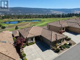 Aerial view of suburban homes with terracotta roofs adjacent to a lush golf course, with a panoramic backdrop of rolling hills and a clear sky.